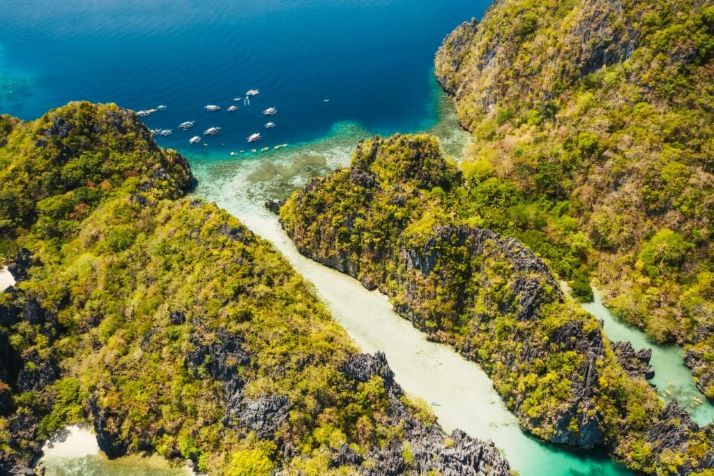 Palawan, Philippines aerial view of tropical Miniloc island. Tourism trip boats moored at entrance to big lagoon Lagoon