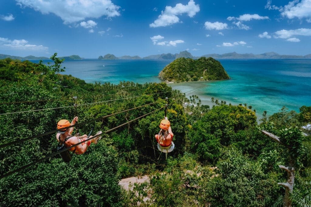 Zipline over Las Cabanas Beach with tourist on sunny day with white clouds over sea. El Nido, Palawan, Philippines Zipline over Las Cabanas Beach with tourist on sunny day with white clouds over sea. El Nido, Palawan, Philippines